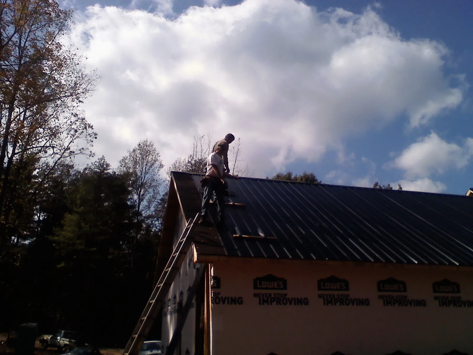 Roofer fastening dark metal panels high against a cloudy sky, from a Roof Inspection job in Villa Park