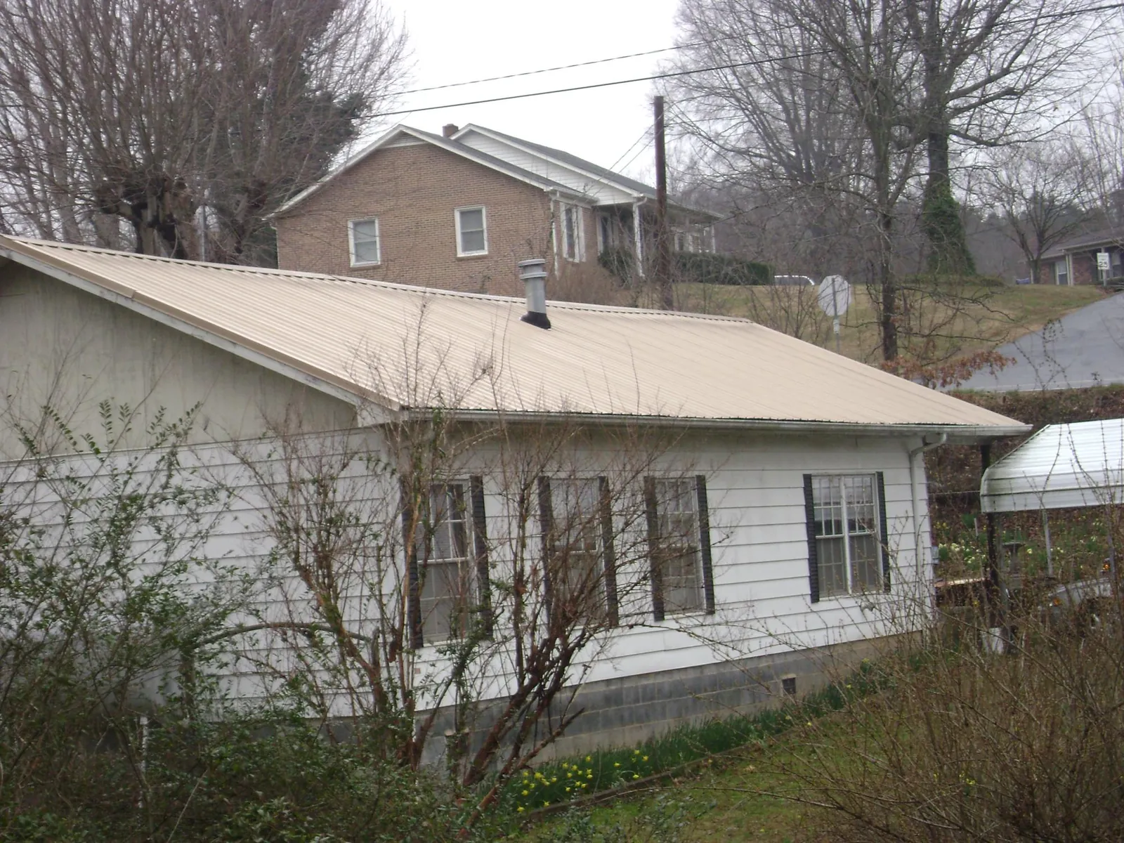 Tan metal roof on a white sided house set into a hillside — Commercial Roofing by Roofing Brothers in Villa Park